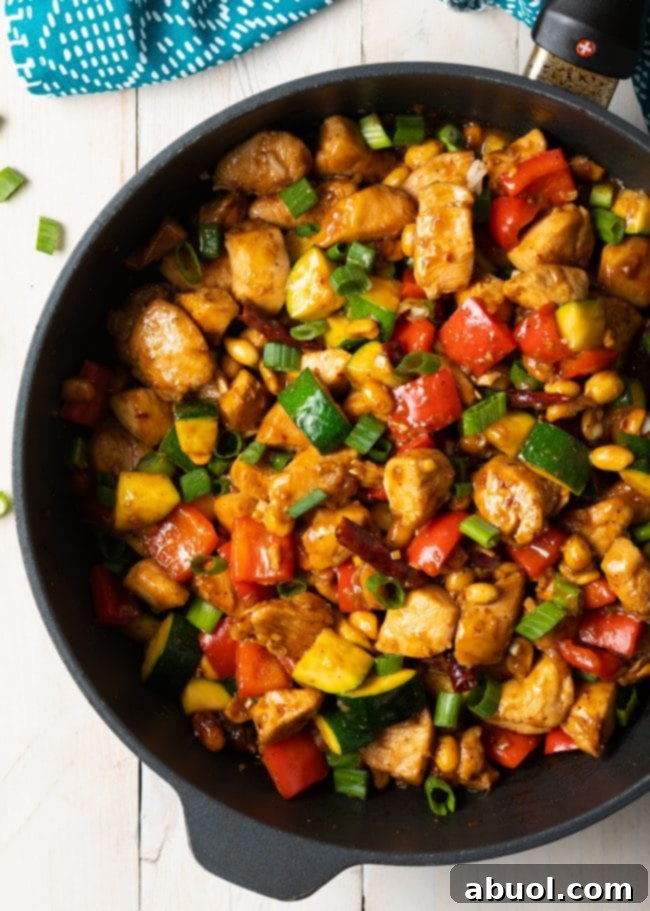 A top-down view of a cast iron skillet bustling with perfectly cooked Kung Pao Chicken: tender chicken pieces, crunchy peanuts, vibrant scallions, zucchini, and bell pepper, all coated in a rich, glossy sauce.