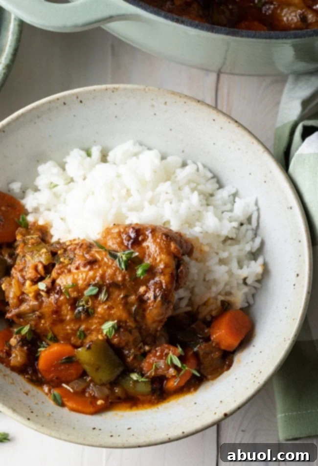 Jamaican brown stew chicken recipe with rice in a bowl, garnished with fresh herbs.