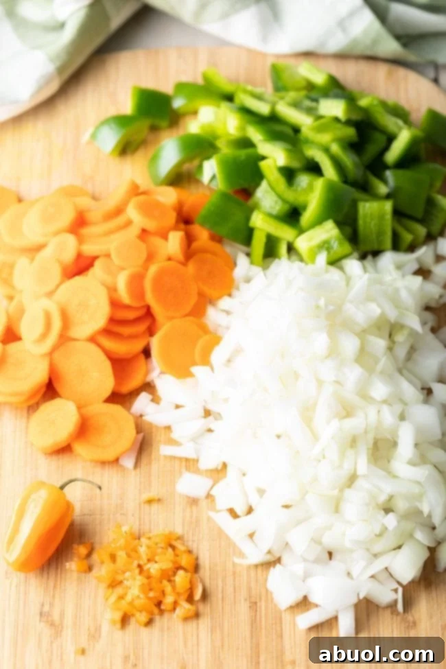 Freshly chopped onions, carrots, and bell peppers on a wooden cutting board, ready for the stew.
