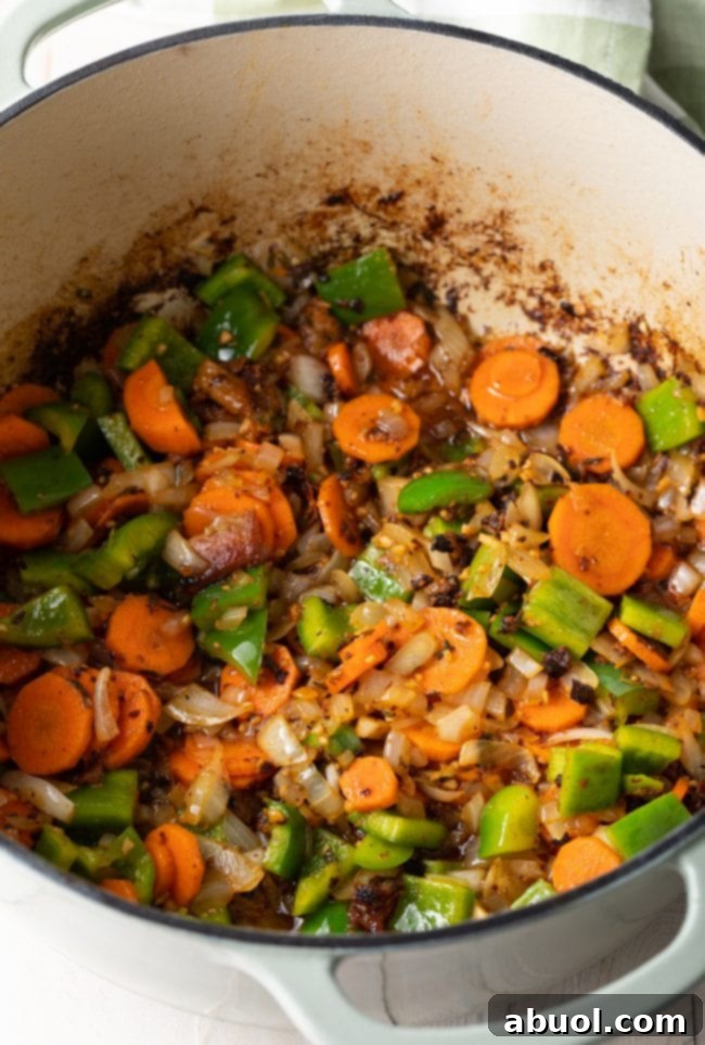 Seasoned and sautéed vegetables (onions, carrots, bell peppers) in a Dutch oven after removing the browned chicken.