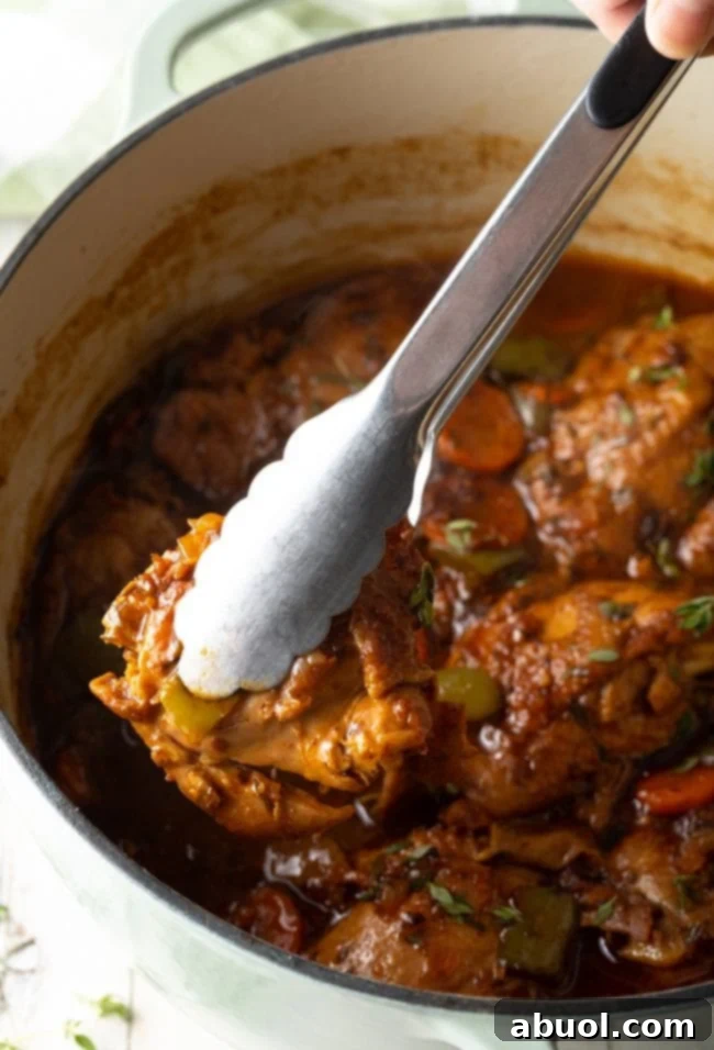 Browned chicken pieces being lifted from a pot with tongs, showcasing their rich color.