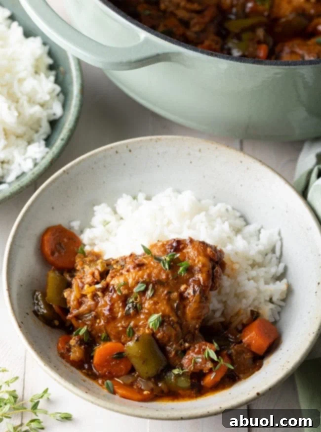 A beautifully plated bowl of authentic Jamaican brown chicken stew with rice, carrots, bell peppers, and fresh seasonings.