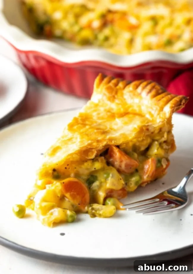 Close-up of a slice of vegetarian pot pie, clearly showing the rich, creamy filling with perfectly cooked carrots, peas, and celery beneath a golden-brown, flaky crust.