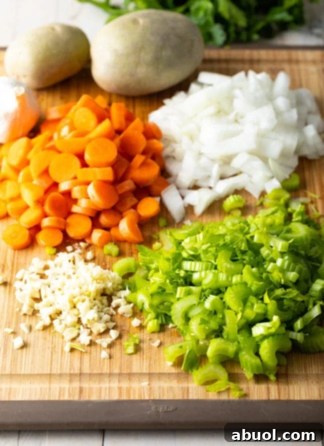 Carrots, onions, celery, and minced garlic diced on a wooden cutting board, meticulously prepared for cooking.
