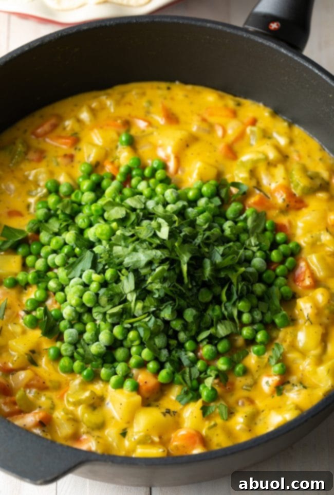 Creamy vegetable filling simmering in a skillet, with frozen peas and fresh cilantro stirred in, creating a rich and vibrant mixture.