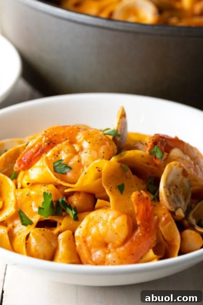 Serving of pappardelle pasta with seafood sauce in a white bowl, garnished with fresh parsley.