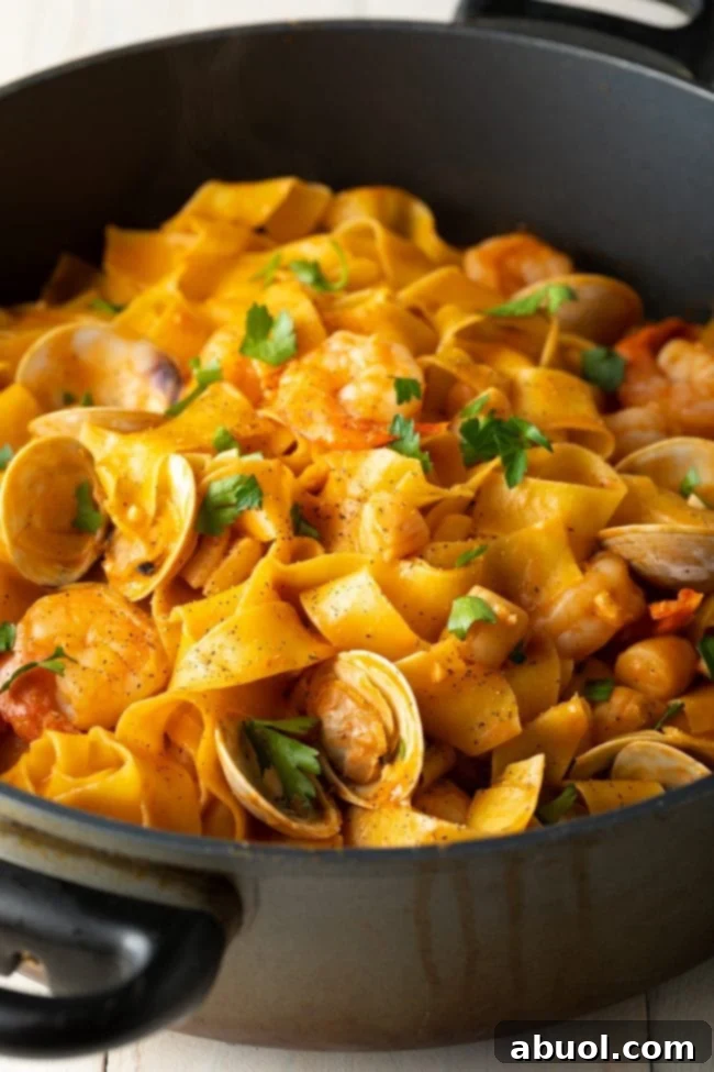 Wide egg noodles with rich seafood sauce, in a black cooking pot.