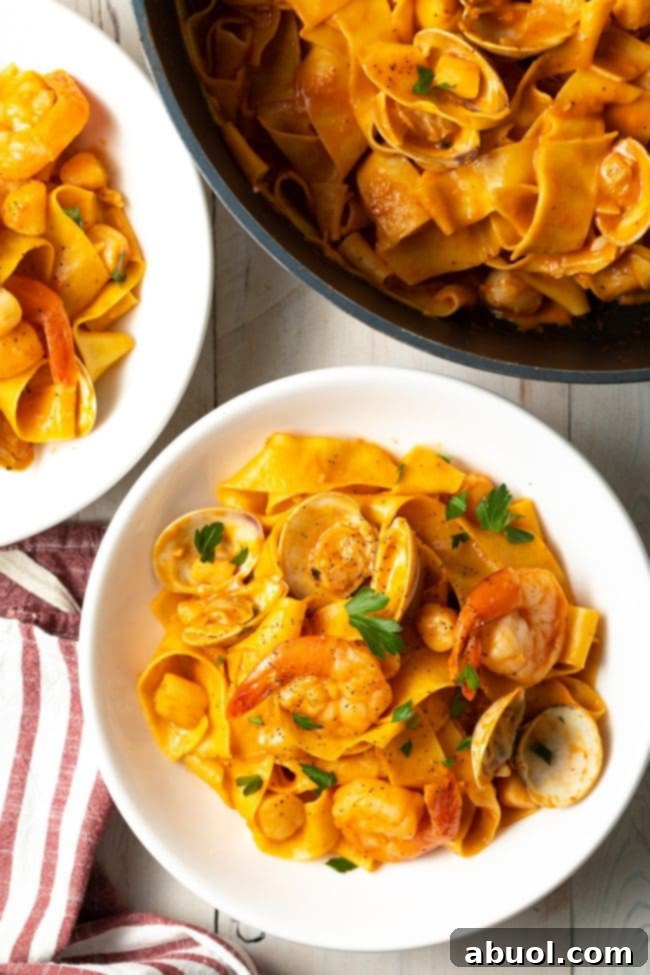 Top down view serving of pappardelle pasta with seafood sauce in a white bowl.