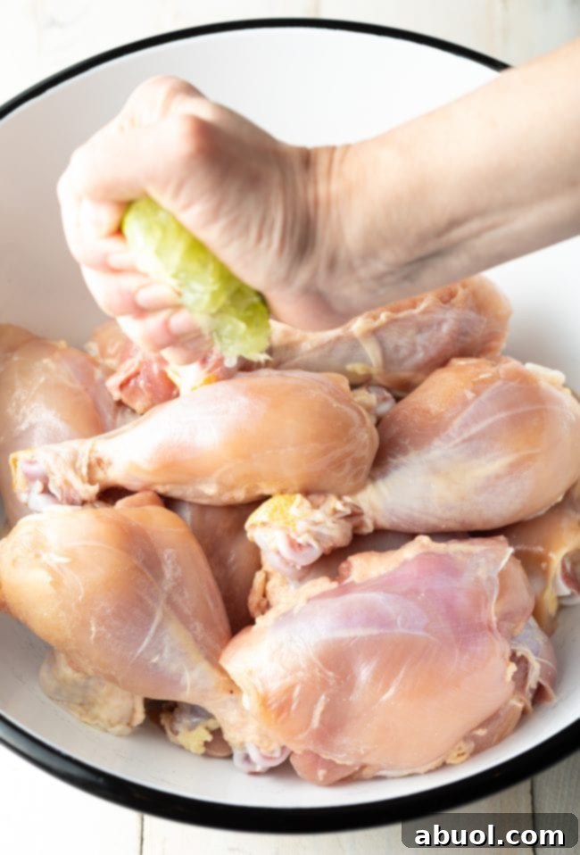 Hands squeezing fresh lime juice over chicken pieces in a mixing bowl, preparing for marination