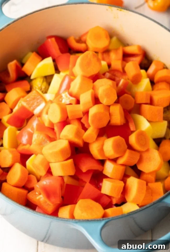 Chopped carrots, bell peppers, and potatoes being added to the pot with chicken and spices