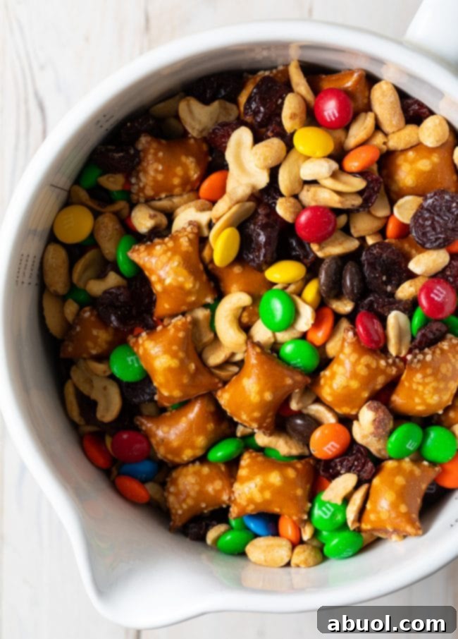 Sweet and salty indulgent trail mix recipe in a white bowl, featuring pretzels, candies, and dried fruit.