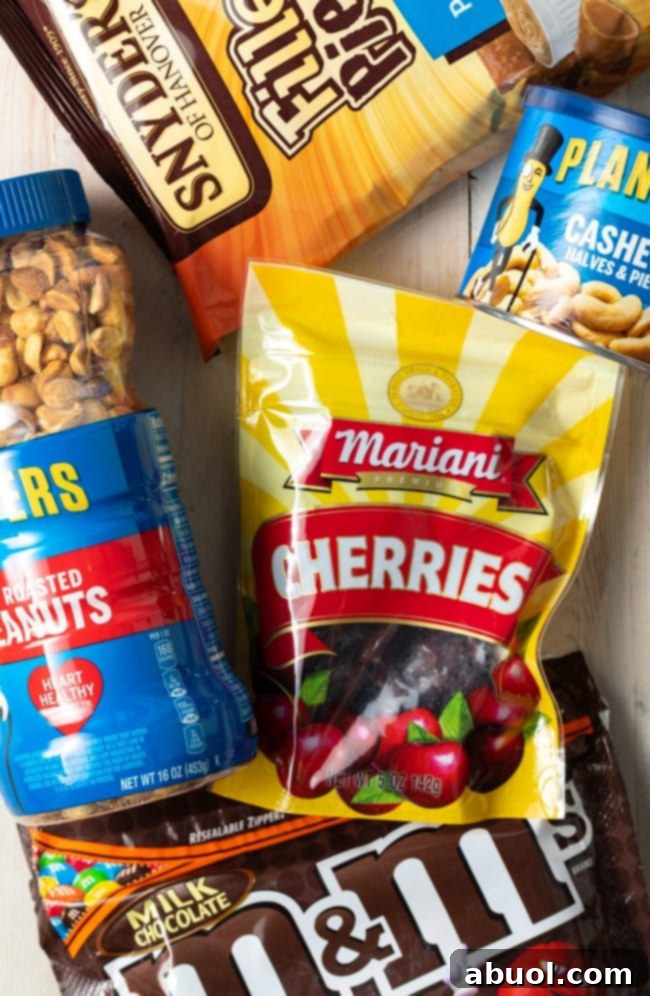 Close-up of indulgent trail mix ingredients: dried cherries, roasted cashews, peanuts, peanut butter pretzels, and colorful M&M candies.