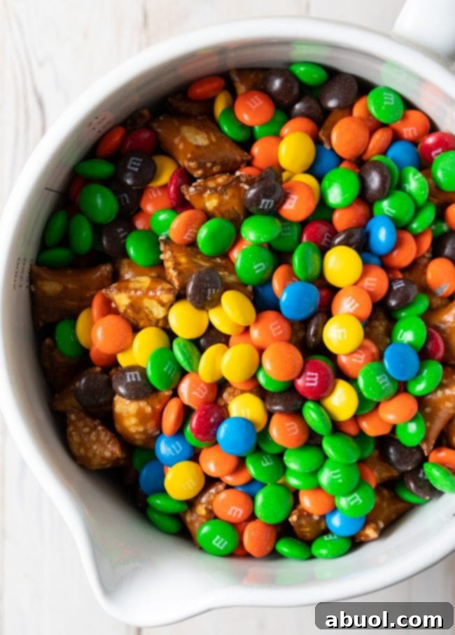 Indulgent trail mix with pretzels, M&M's, and dried cherries in a white bowl.