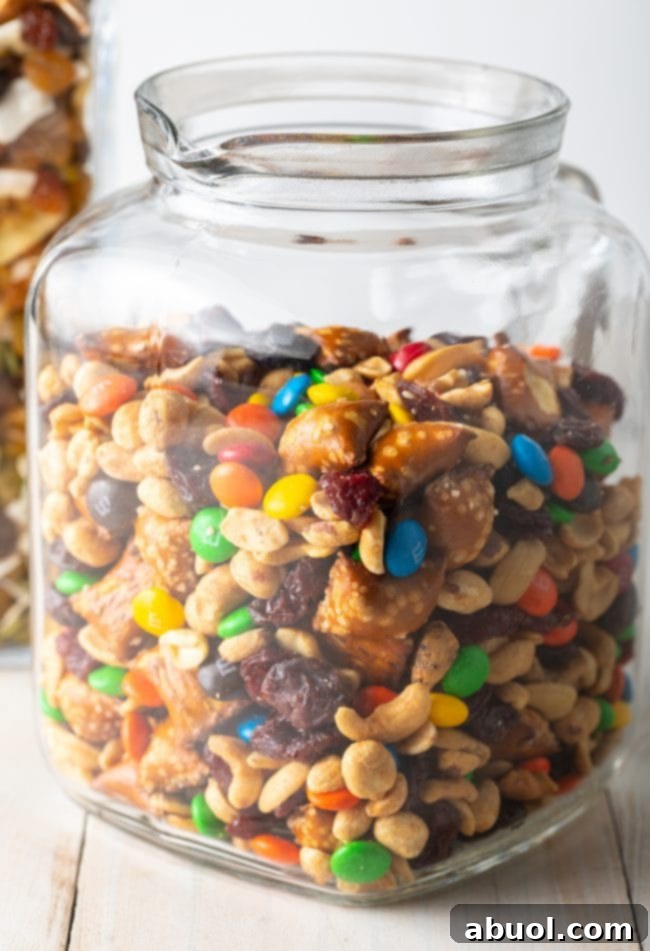 A side view of a glass jar filled with indulgent trail mix, showcasing the colorful mix of sweet and savory components.
