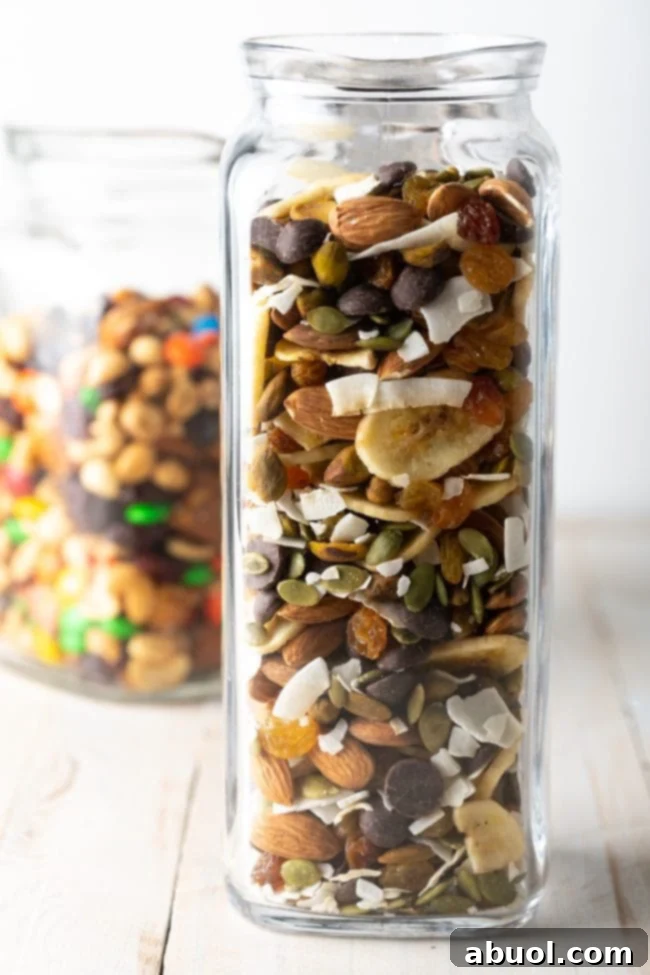 Homemade trail mix recipe featuring banana chips, unsweetened coconut, various nuts, and seeds in a glass jar, ready for snacking.