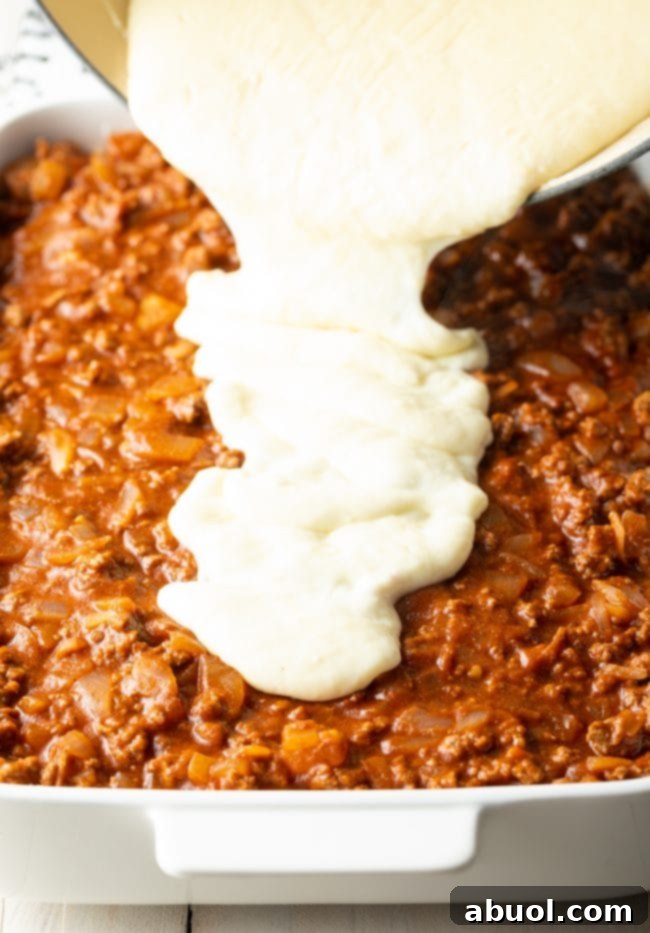 Pouring creamy bechamel sauce over the meat sauce.