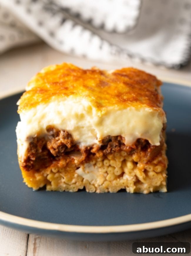 Square of Greek lasagna with bucatini pasta and creamy bechamel sauce, on a gray plate.