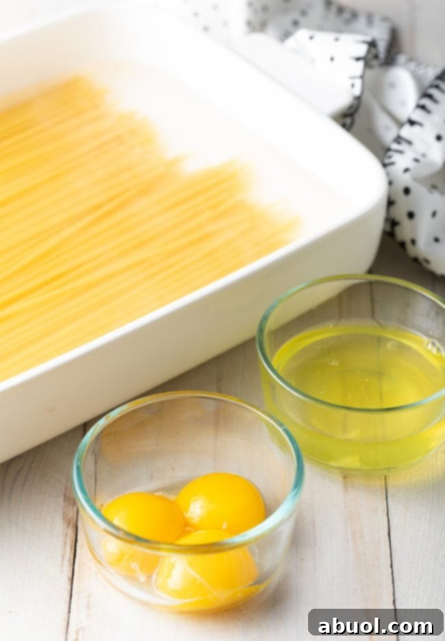 Bucatini pasta in a white baking dish, glass bowl with egg yolks and separate glass bowl with egg whites.
