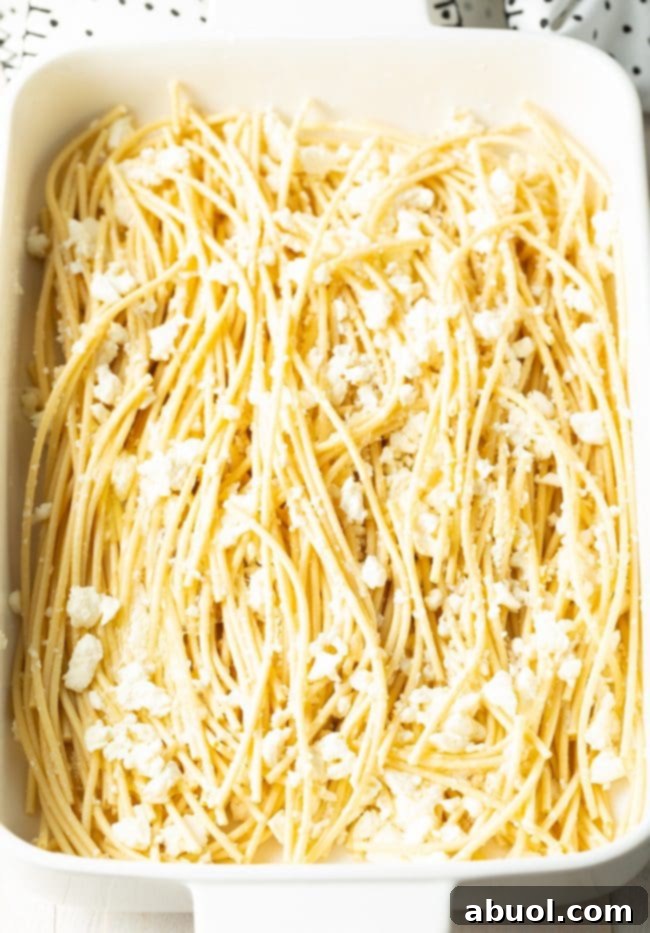 Soaked bucatini in a white baking dish, topped with crumbled Greek feta cheese.