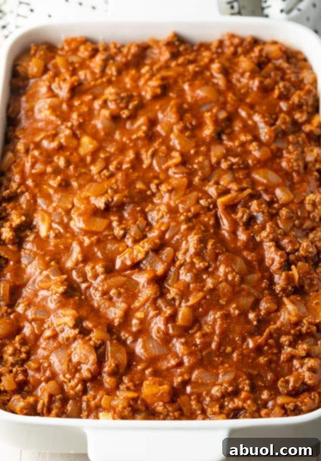 Zesty tomato meat sauce poured on top of pasta in a white baking dish.