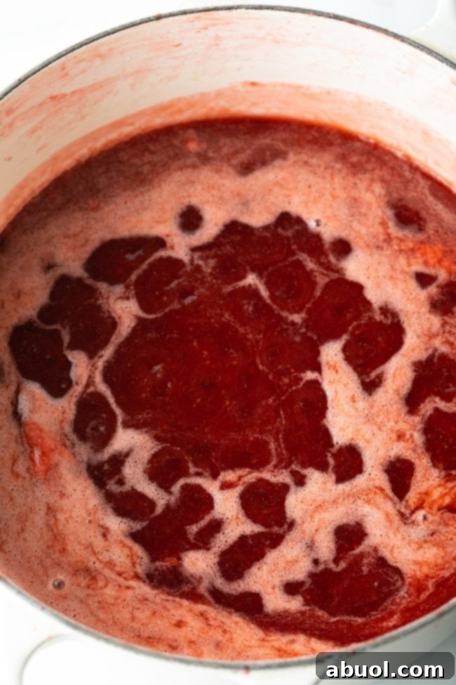 Homemade strawberry rhubarb jam mixture simmering gently in a large pot on the stove