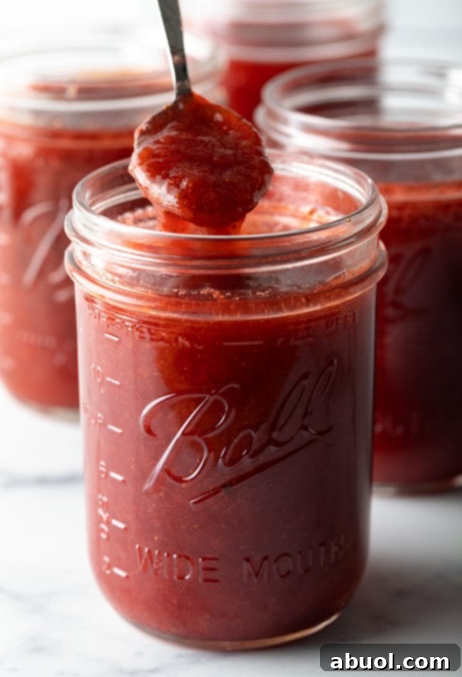 A scoop of rich strawberry rhubarb freezer jam being lifted from a jar, showing its luscious texture