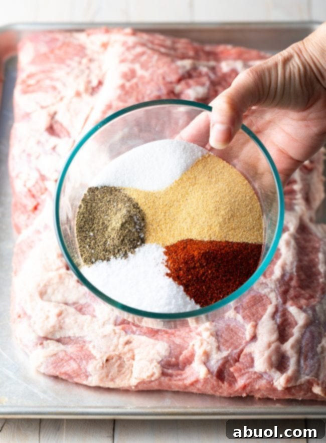 Dry-Brined Smoked Brisket 6 A glass bowl of dry brine spices being sprinkled over a raw whole packer beef brisket on a baking sheet, ready for seasoning.