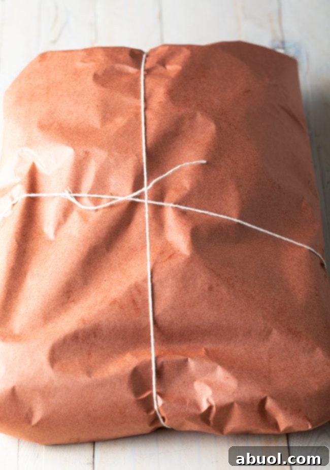 Dry-Brined Smoked Brisket 9 A large piece of beef brisket, expertly wrapped in pink butcher paper and secured with kitchen twine, ready to continue smoking.