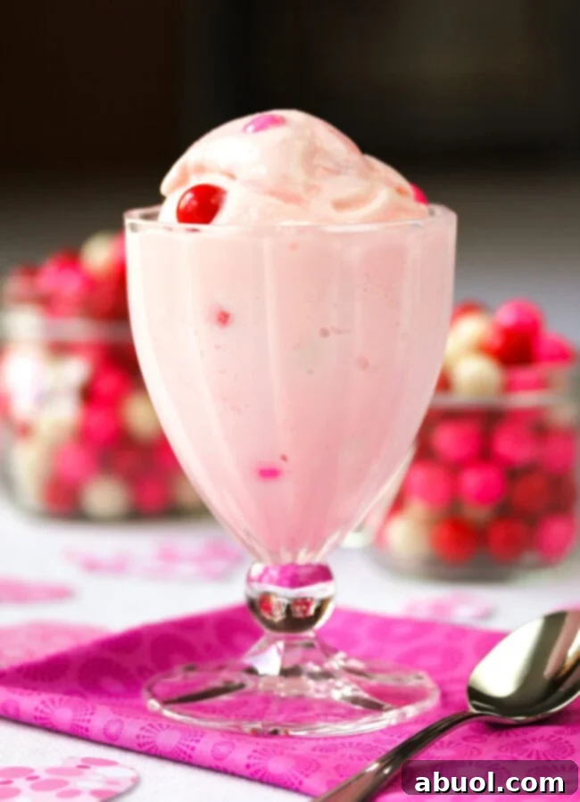 A elegant glass bowl showcases a scoop of Baskin Robbins-style pink bubblegum ice cream, artfully garnished with colorful gumballs and a fresh cherry.
