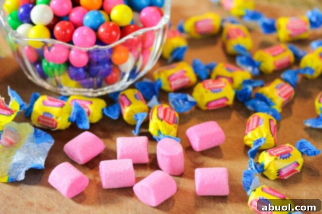 A clear glass bowl filled with an assortment of colorful round gumballs, with several unwrapped pieces of classic pink bubble gum nearby, ready for inclusion in the ice cream.