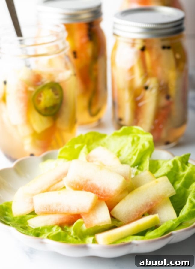 Sliced pickled watermelon rinds served neatly on a small plate alongside fresh lettuce leaves.