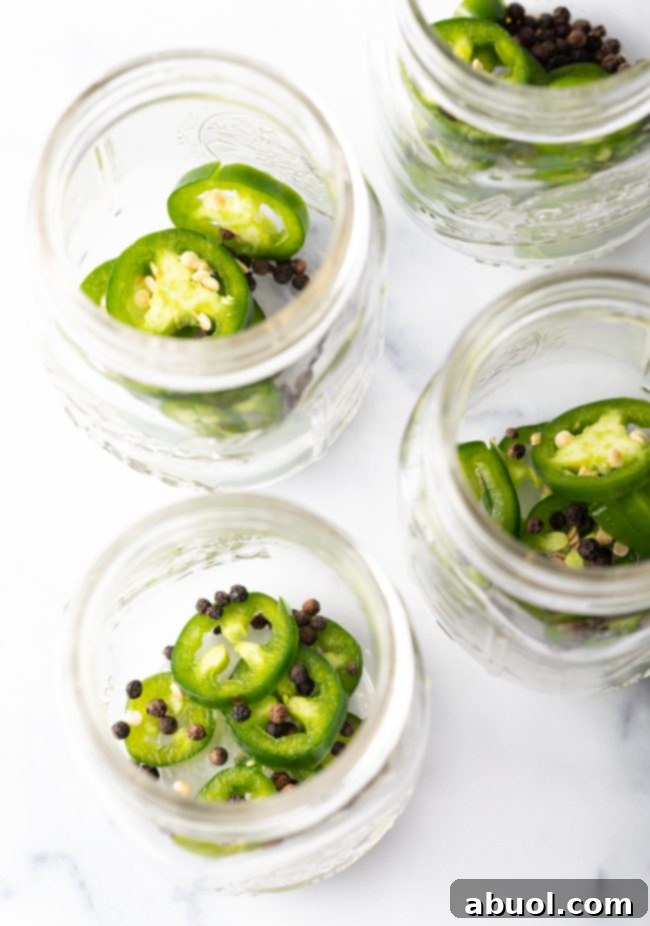 Glass jars with pre-placed jalapeño slices and black peppercorns at the bottom.