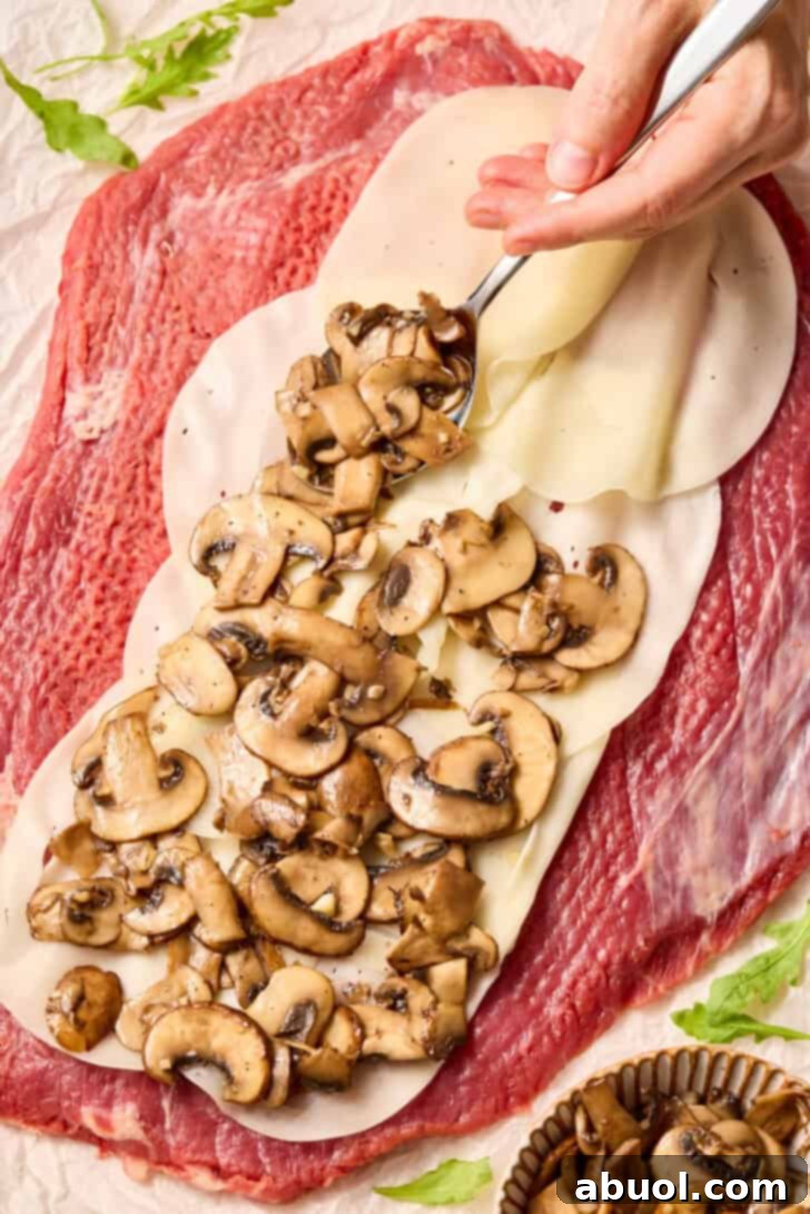 Pounded flank steak laid out on a cutting board, ready to be layered with cheese and mushrooms.