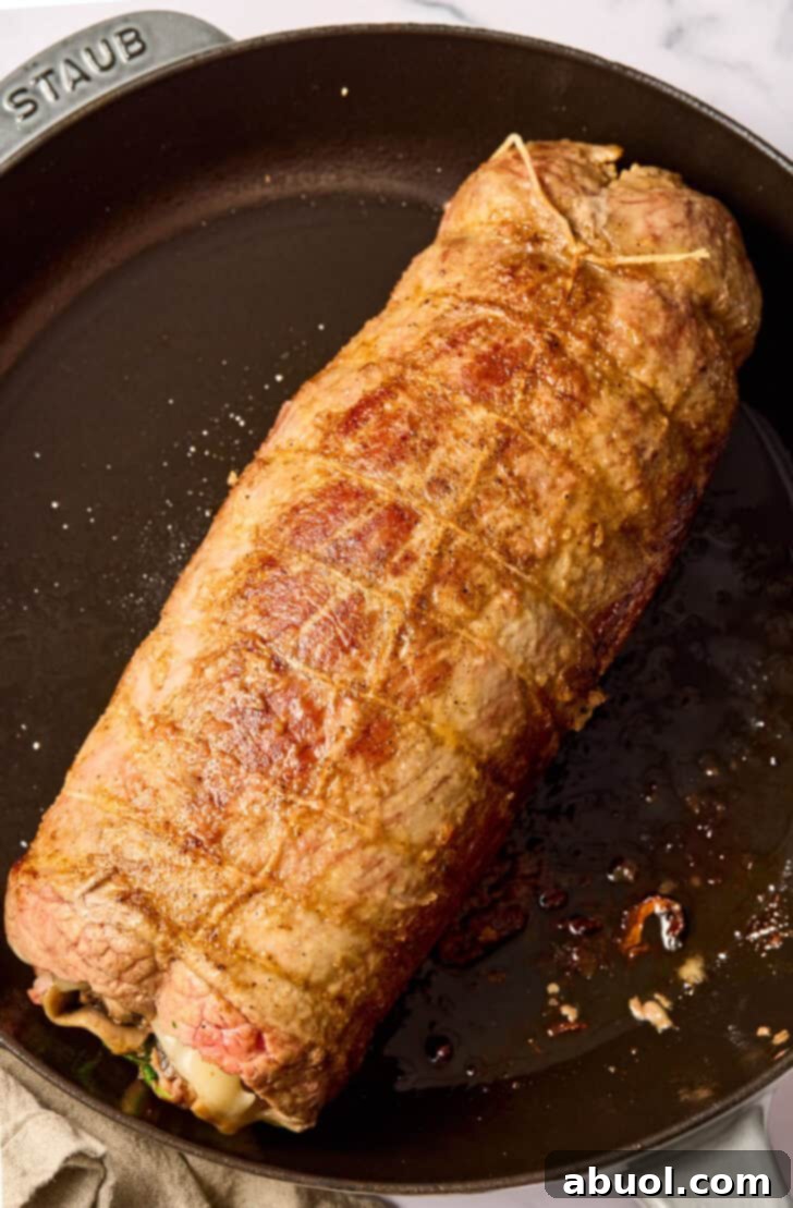 Stuffed flank steak being seared to a golden brown in a cast iron skillet.