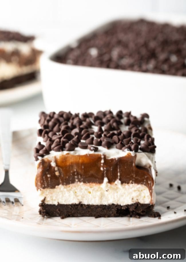 Close-up slice of no-bake chocolate lasagna on a plate, showing distinct layers of Oreo crust, cream cheese, chocolate pudding, and whipped topping.