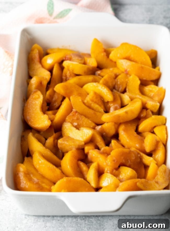 Sliced fresh peaches layered in a baking dish, ready for the cobbler batter