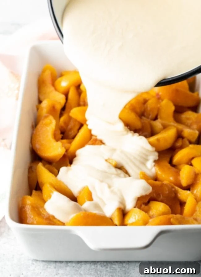 Pouring Bisquick batter over the spiced peach fruit mixture in a baking dish