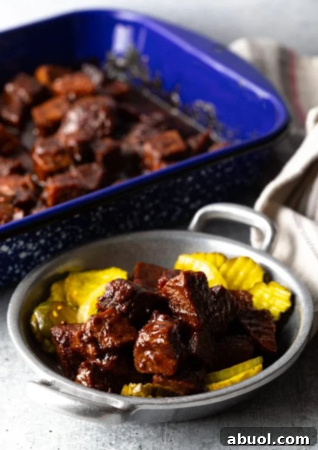 Oven-Baked Brisket Burnt Ends 10 Chunks of brisket burnt ends in a metal bowl with sliced bread and butter pickles.