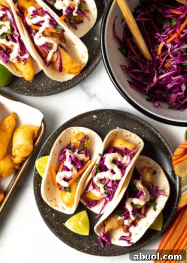 overhead view of 3 fried fish tacos with more fried fish, slaw, and baja sauce on the sides. 