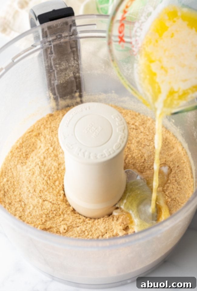 Graham cracker crumbs in a food processor with melted butter being poured on top.