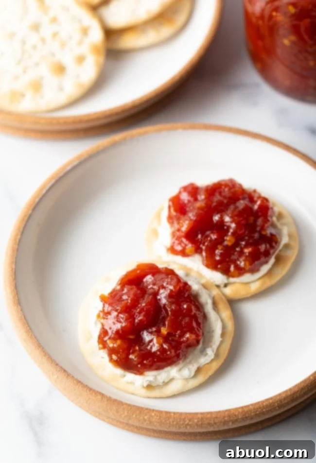 An overhead view of a simple white plate featuring two crackers, elegantly topped with creamy cheese and a dollop of this irresistible tomato jam recipe.