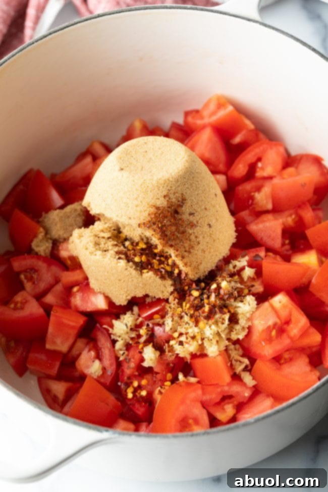 A pot filled with chopped tomatoes, brown sugar, and an array of fragrant spices, ready to be cooked down into jam.