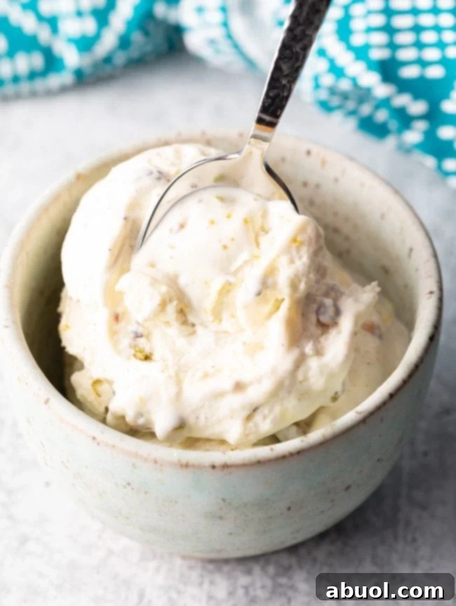 A spoon scooping creamy, saffron-infused kulfi ice cream from a bowl, garnished with chopped pistachios.