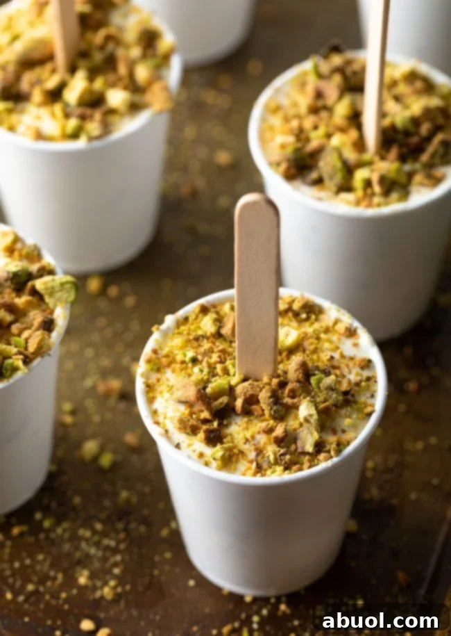 A homemade Indian kulfi ice cream pop, generously coated with crushed pistachios around its base.