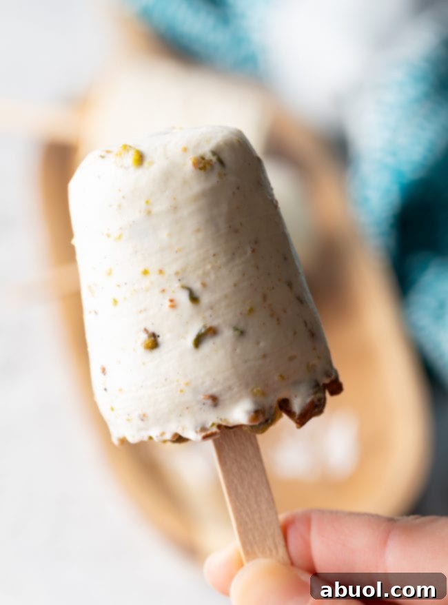 Close-up of a single pistachio saffron kulfi ice cream pop on a wooden stick, showcasing its creamy texture.