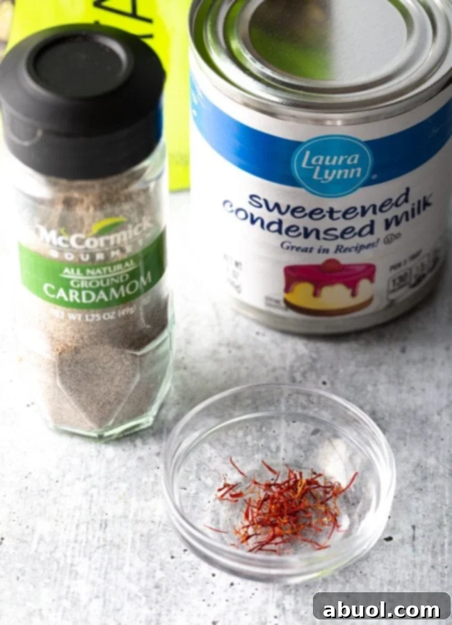 Close-up of key Kulfi ingredients: cans of sweetened condensed milk, a bowl of ground cardamom, and saffron threads.