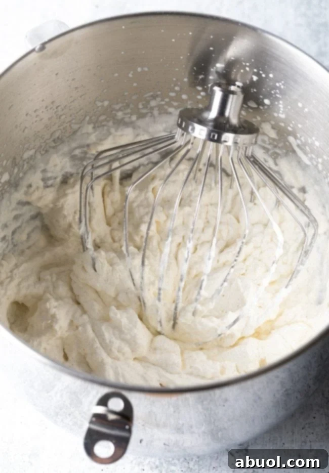 Close-up of a standing mixer with a wire whisk attachment, whipping heavy cream into firm peaks.