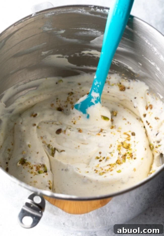 Close-up of chopped pistachios being gently folded into the Kulfi ice cream base with a rubber spatula.