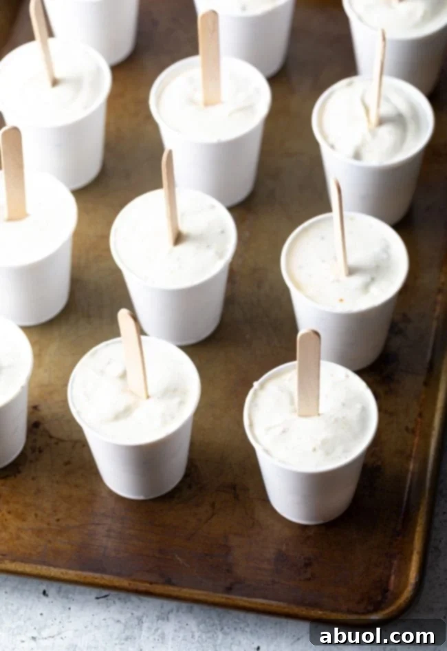 Small paper cups filled with Kulfi mixture, each with a popsicle stick inserted, ready for freezing.