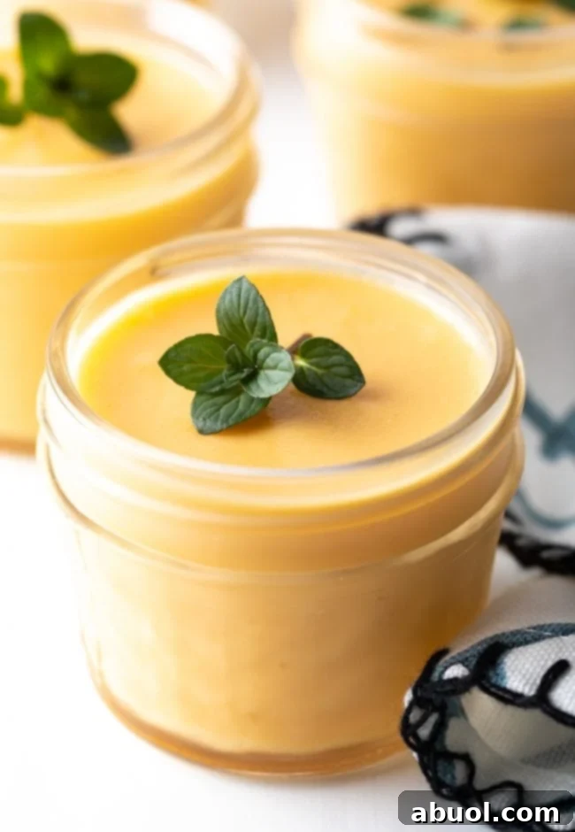 Close-up of vibrant yellow dairy-free mango pudding in a glass cup, garnished with fresh green mint leaves.